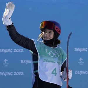 Eileen Gu with arm raised to wave at the crowd after winning Gold.