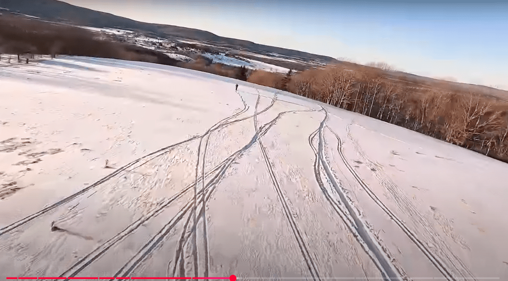 Screenshot of aerial footage showing a snowfield in West Virginia with criscrossing ski tracks. From 'Freeland ~ A White Grass Story'