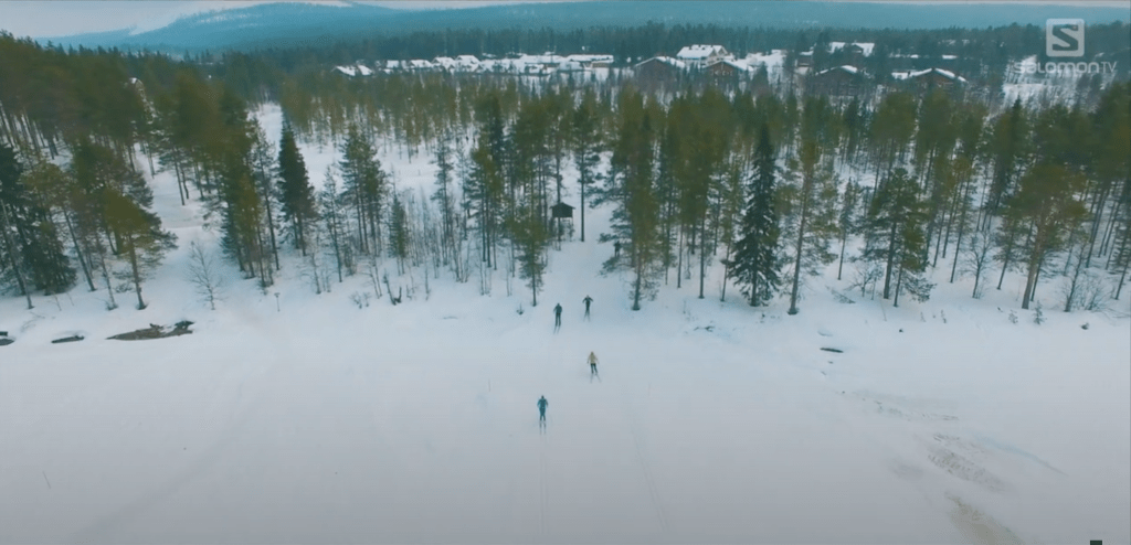 Screenshot of aerial footage showing a skiers exiting an evergreen forest in Lapland Finland.. From 'Lapland | Salomon TV'